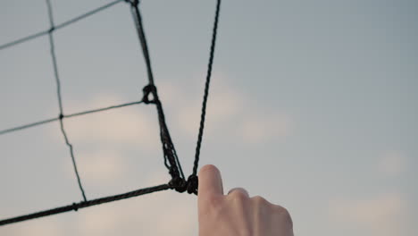 close-up of volleyball net held by someone in green clothing checking its firmness with hazy sky in the background, highlighting the net's structure