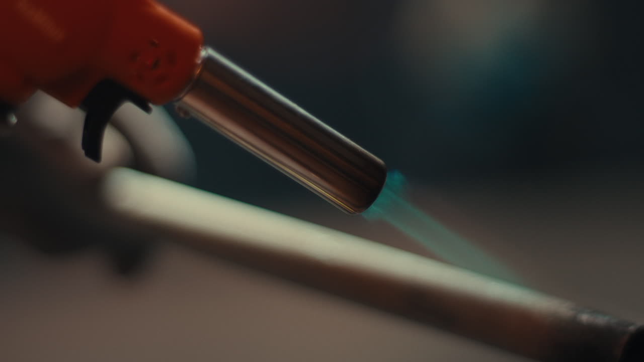 Primo piano di un cannello che riscalda una barra di metallo producendo una fiamma blu, rotazione al rallentatore, dettagli astratti.