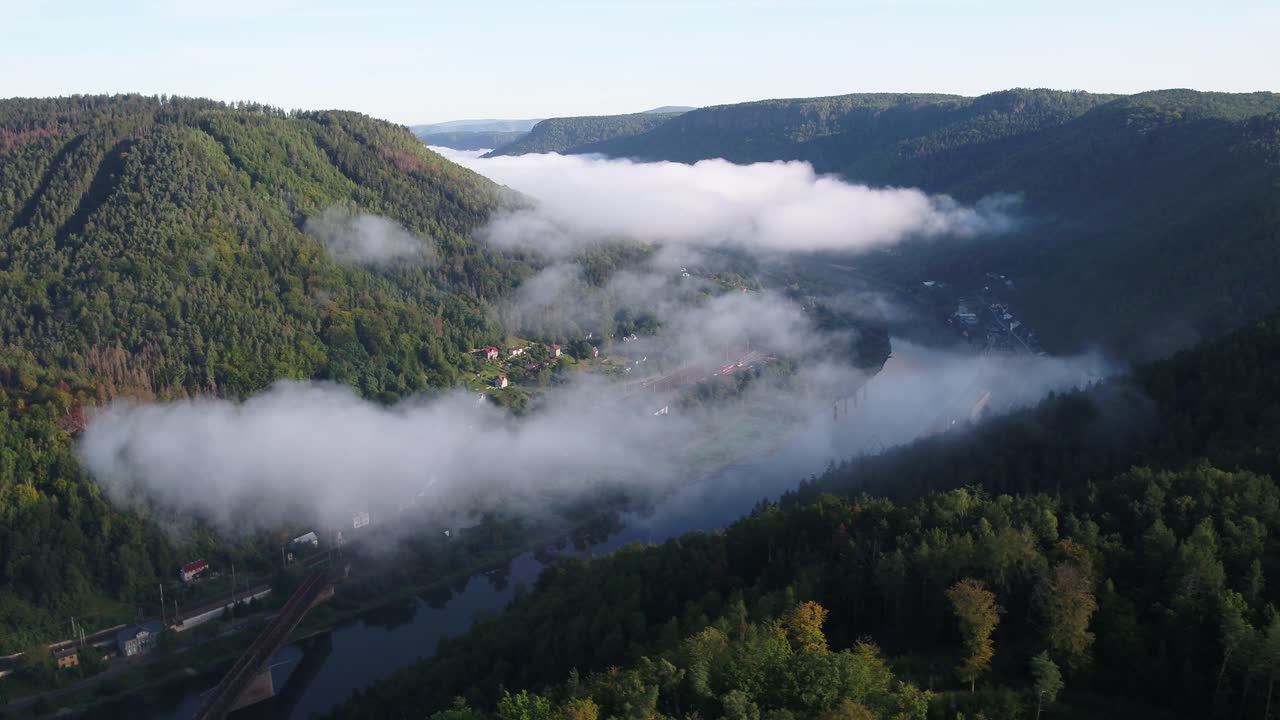 Drone zooms out revealing dense morning fog flowing through the Elbe valley near Decin, surrounded by lush green hills