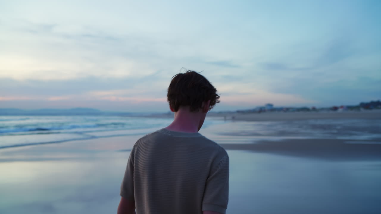 Giovane uomo che cammina sulla spiaggia al tramonto