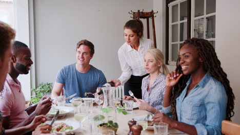 camarera sirviendo vino a un grupo de amigos comiendo en un restaurante juntos