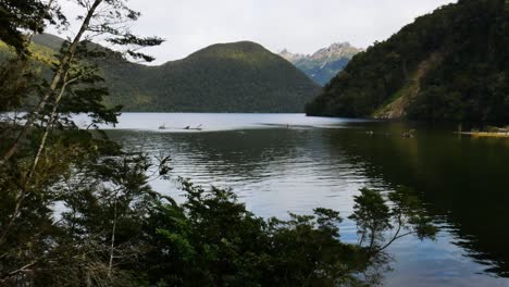 Idyllic-lake-surrounded-by-vegetated-mountains-during-bright-sky-in-New-Zealand--Wide-shot