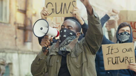 homem afro-americano com lenço no rosto gritando em um alto-falante em um protesto com grupo multiétnico de pessoas na rua