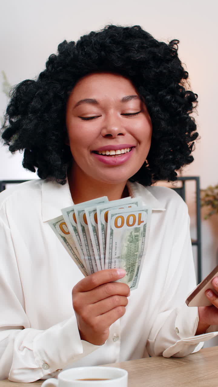 African american businesswoman surprised counts cash holding smartphone planning spending big profit