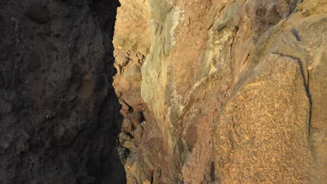 Sunlight-shines-on-rocky-cliff-coast-at-golden-hour,-close-up,-tilt-up,-Tenerife