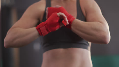 mid section of caucasian female boxer wrapping boxing tape on her hands at the gym