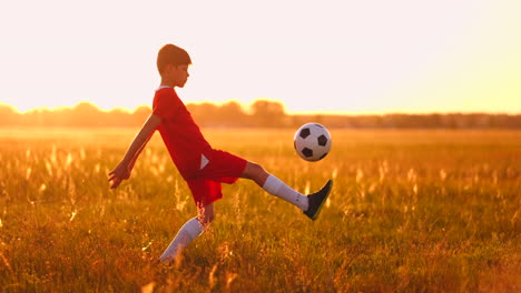 Ein-Junger-Junge-In-Einem-Roten-T-Shirt-Und-Turnschuhen-Jongliert-Bei-Sonnenuntergang-Mit-Einem-Fußball-Und-Trainiert-Und-Bereitet-Sich-Darauf-Vor,-Fußballspieler-Zu-Werden.-Der-Weg-Zum-Traum.-Harte-Arbeit