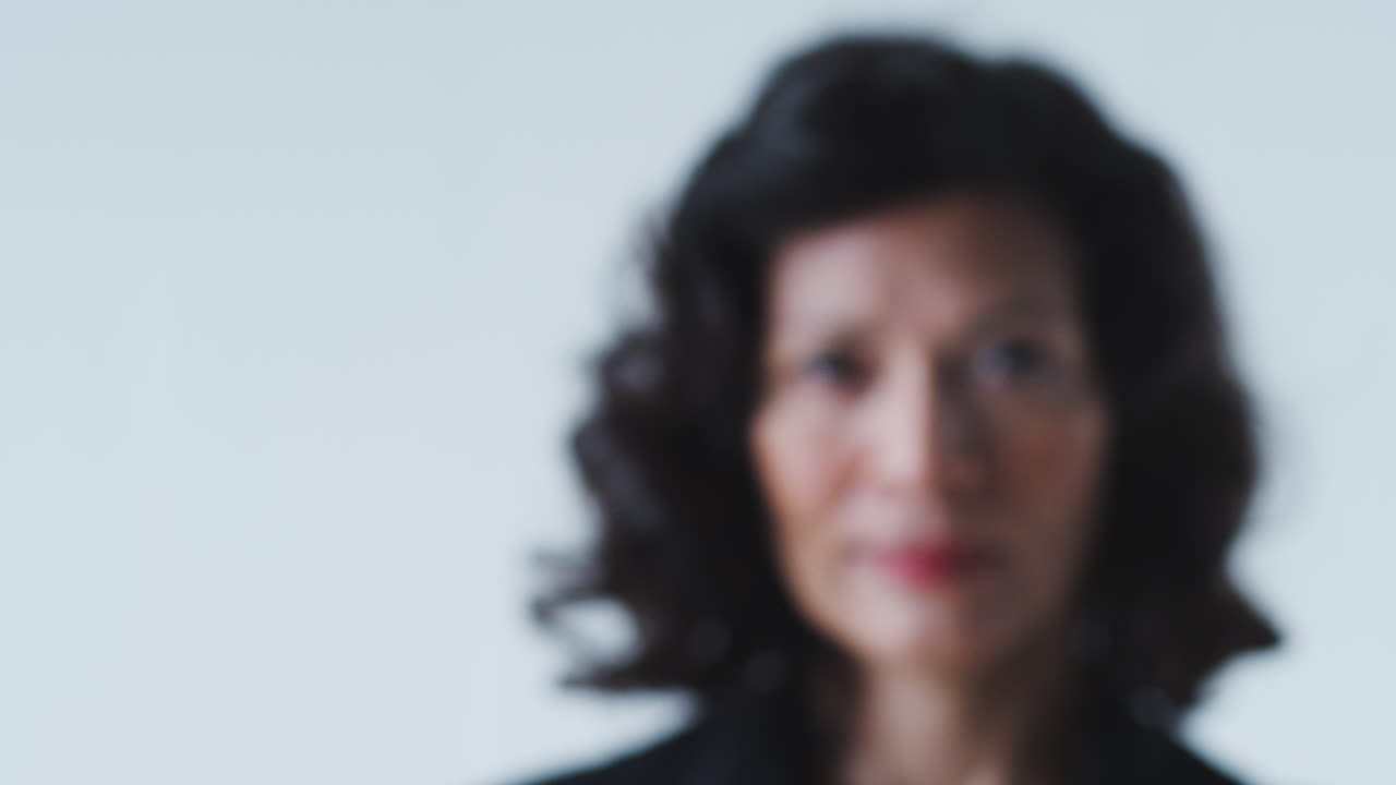 tire el retrato de enfoque de una mujer de negocios madura sonriente en traje de pie contra la pared blanca del estudio