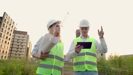 dos ingenieros industriales usan casco de seguridad y sostienen la ingeniería de tableta trabajando y hablando con la inspección de dibujos. en la construcción afuera. herramientas de ingeniería.