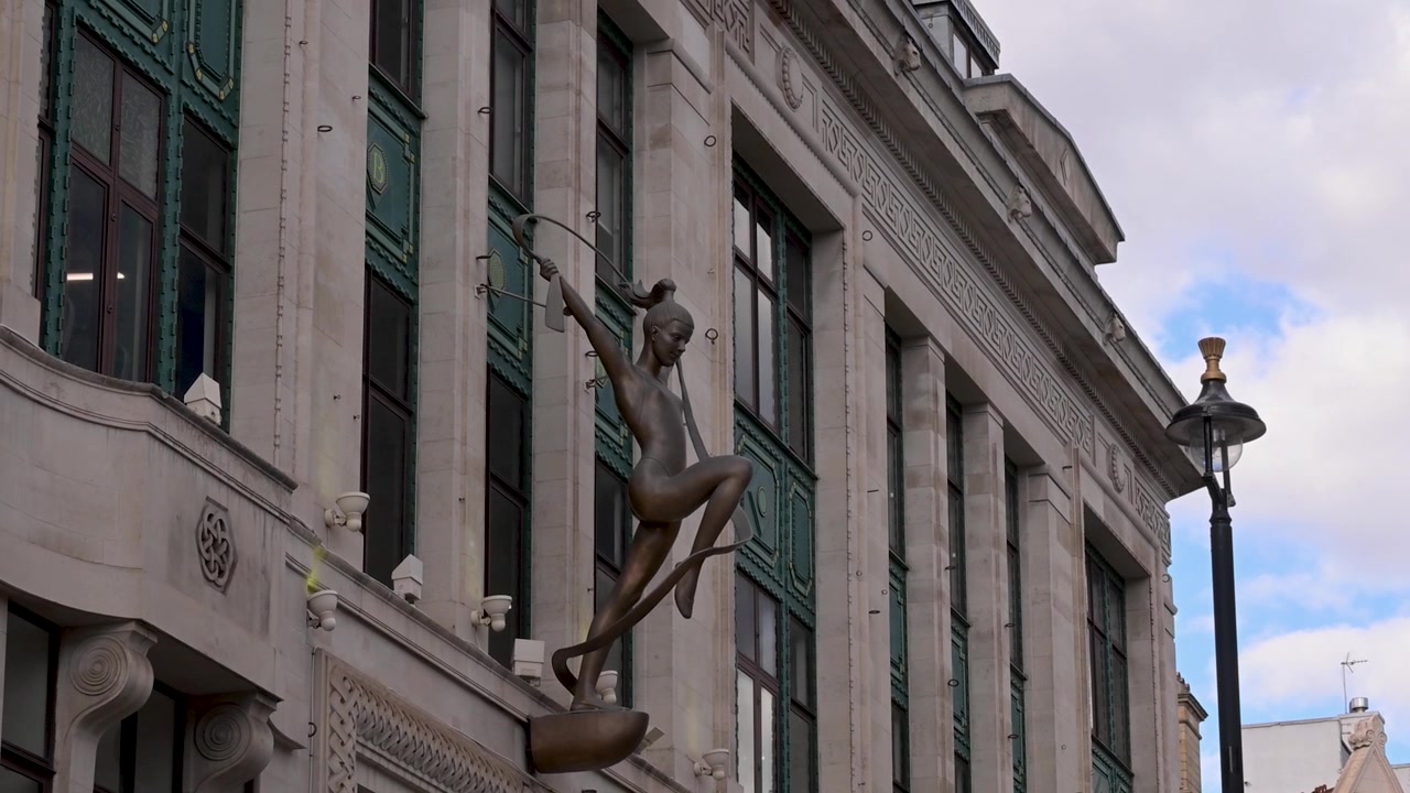 Scultura di ballerina in bronzo con nastro incorniciata contro alte finestre in pietra su una strada cittadina nuvolosa