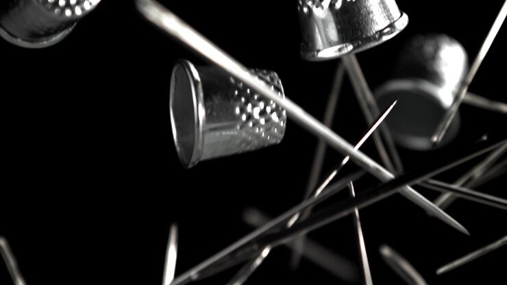 Metallic Sewing Thimbles and Needles Falling in Slow Motion