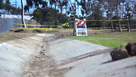 an empty desolate park enclosed by a chain link fence where the wind blows caution tape attached to a construction barrier just off a cement path