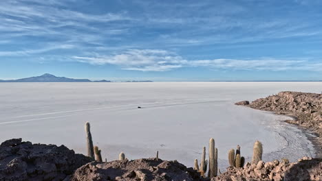 pan across salt flats of bolivia as car drives below cactus covered mountain