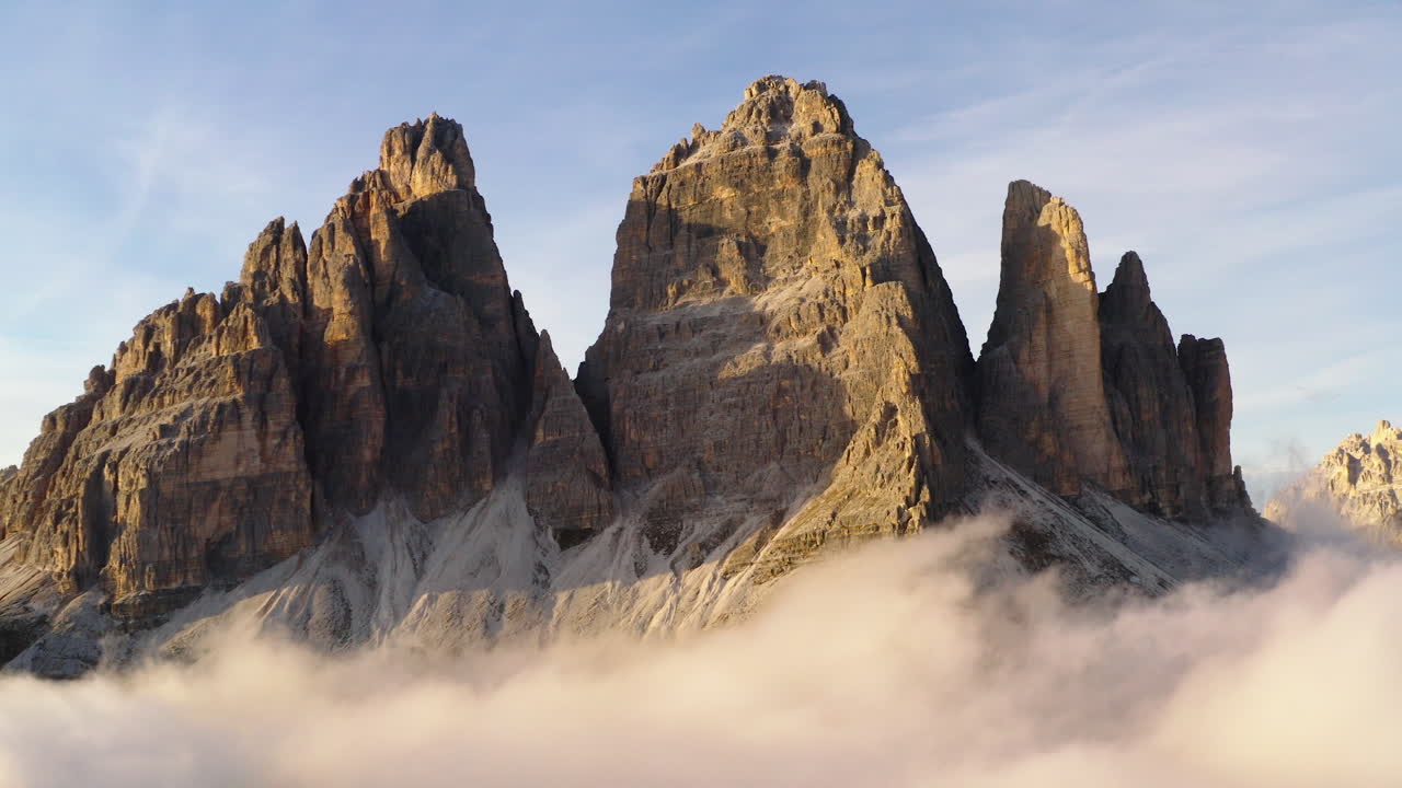 일출 때 공중에서 궤도를 도는 미묘한 빛나는 구름에서 떠오르는 햇볕에 쬐인 트레 치메 사우스 티롤 산봉우리