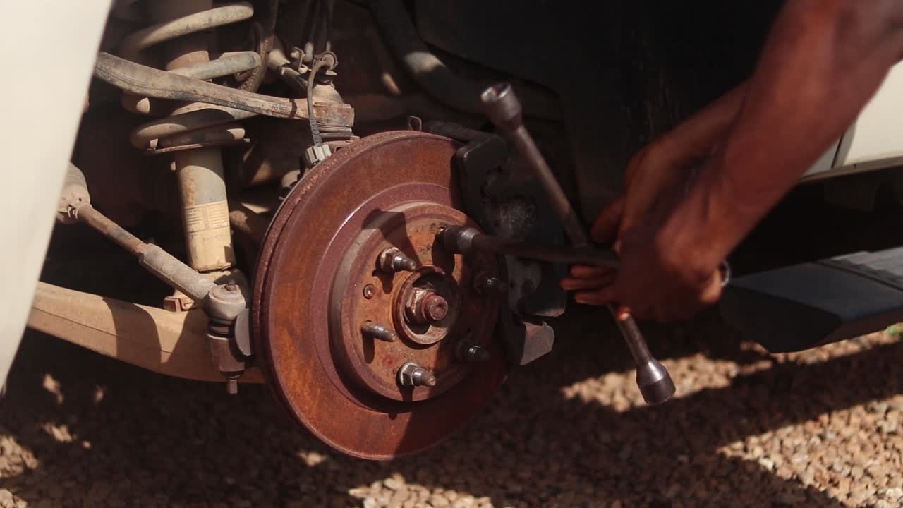 A mechanic loosens a car wheel rotor lug nut with a cross lug wrench and removes it by hand