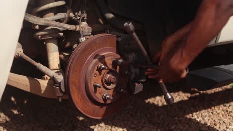 a mechanic loosens a car wheel rotor lug nut with a cross lug wrench and removes it by hand