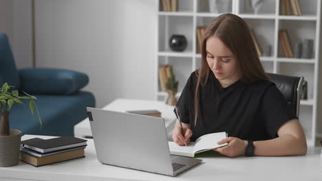 female student is making notes of online webinar viewing on screen of laptop self-education and e-learning writing in notebook