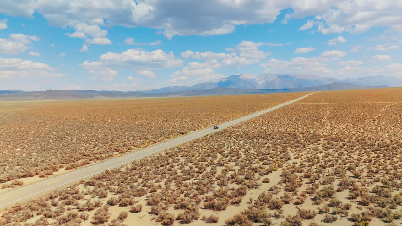 Long straight road in the lifeless desert. Highway to Nevada from California. Beautiful landscape at backdrop of blue skies with white clouds.