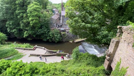 view looking down onto historic old mills with railway tracks to the right and all surrounded by green trees moving and old structures