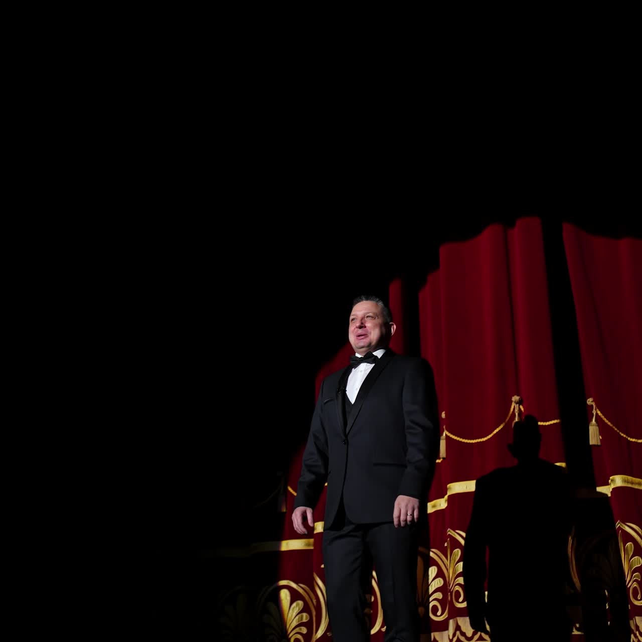 Senior man in costume on stage in darkness. Actor man in selective light on stage during the performance in the theater