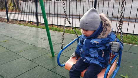 caucasian toddler swinging outdoors. baby boy in warm clothes swinging on the playground.