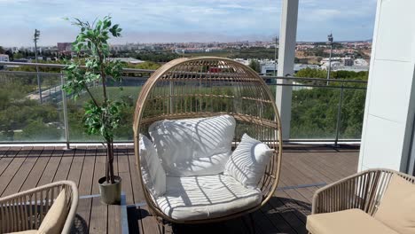 resting on a terrace with a wicker chair and cushions, offering a city view, all without people