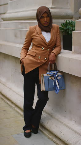 Vertical-Video-Full-Length-Portrait-Of-Muslim-Businesswoman-Wearing-Hijab-And-Modern-Business-Suit-Standing-Outside-City-Office-Buildings-4