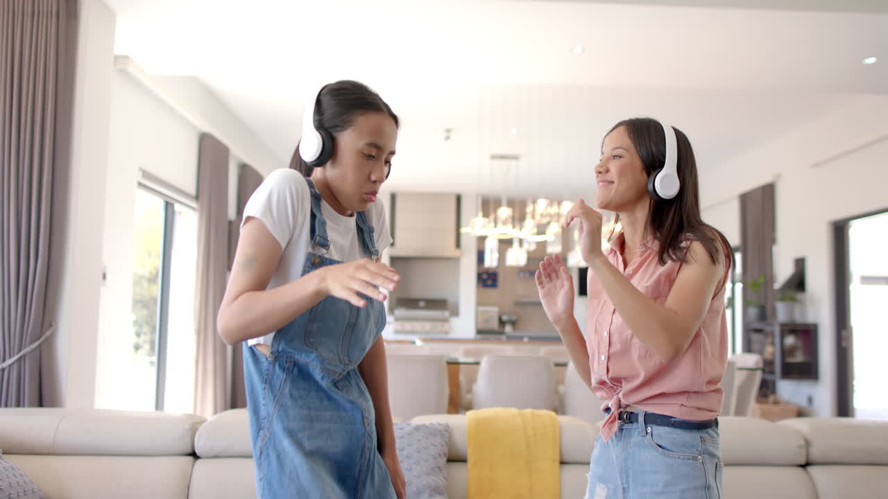 Dancing together, two teenage girls wearing headphones enjoying music indoors