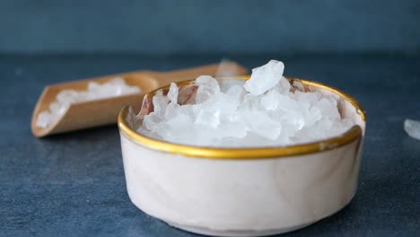 close-up of a bowl of white sea salt crystals with a wooden scoop