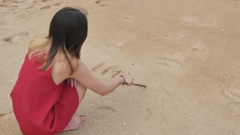 young-asian-woman-write-text-"I-MISS-U"-on-the-white-sand-beach