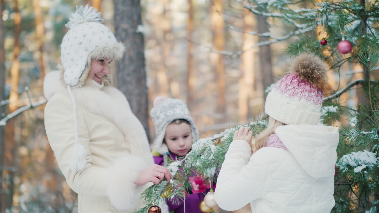 두 자매와 어머니는 겨울에 새해 장난감으로 집 안뜰에 있는 전나무를 장식합니다