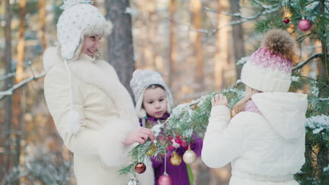 dos hermanas y su madre decoran el abeto en el patio de la casa con juguetes de año nuevo en invierno