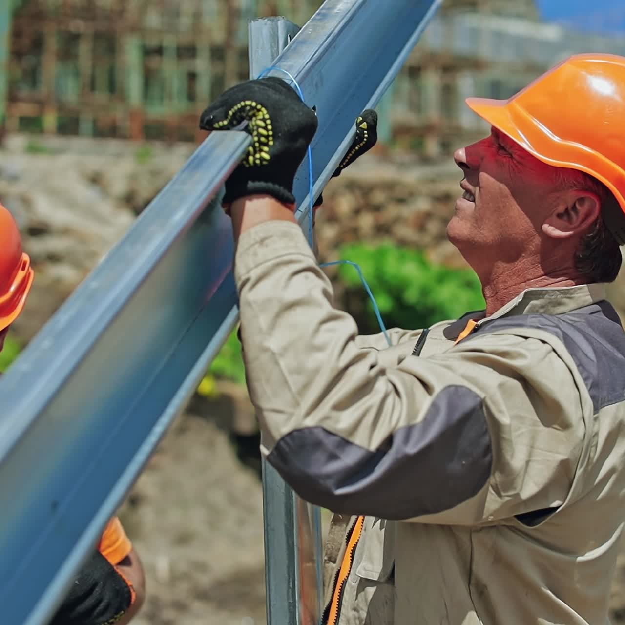 Solar panel technicians install metal frame. Workers in orange helmets making metal basis for solar system on the field. Close-up.