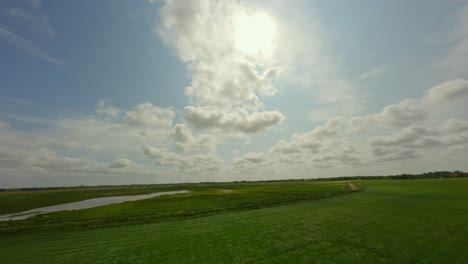 drone flying low above the grass fields towards the sky showing the sun and the clouds