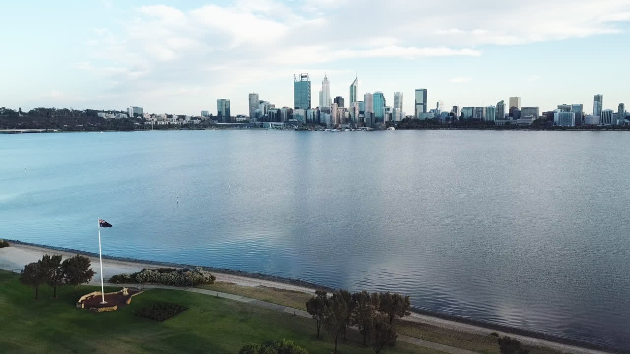 panorámica aérea del asta de la bandera australiana junto al agua, el horizonte de la ciudad de perth en segundo plano.