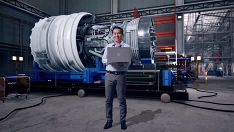 full body of an asian male professional worker standing with his laptop with airplane engine maintenance conducted, analytics checking the turbine, he is looking at the camera with a smile