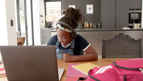 happy african american girl using headphones and laptop raising hand in online class, slow motion