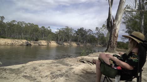 Blonde-woman-comes-and-sits-on-chair-camping-on-river