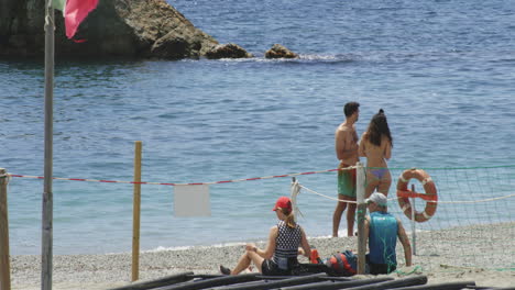 tourists at fegina beach with waving flag in monterosso al mare, italy. tilt-up shot