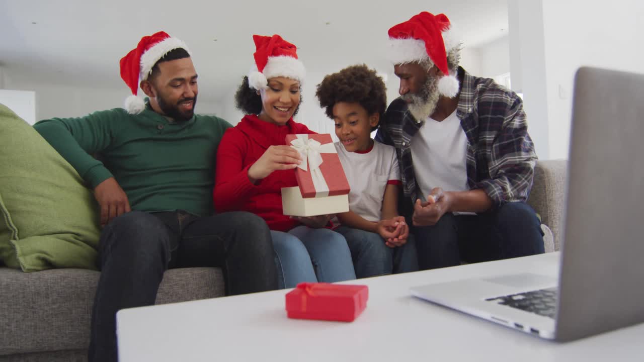 familia multigeneracional abriendo una caja de regalos mientras tiene una videochat en su computadora portátil