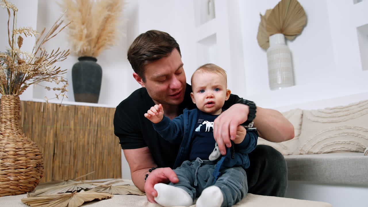 Little child holding black beads bracelet in hands. Father takes away the toy from kid giving him a pacifier.