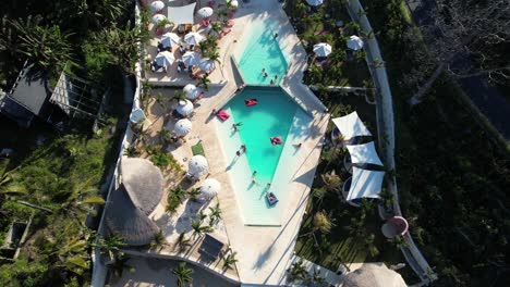 top down flying over swimming pool lounge of cactus beach club resort in nusa penida island, indonesia - aerial