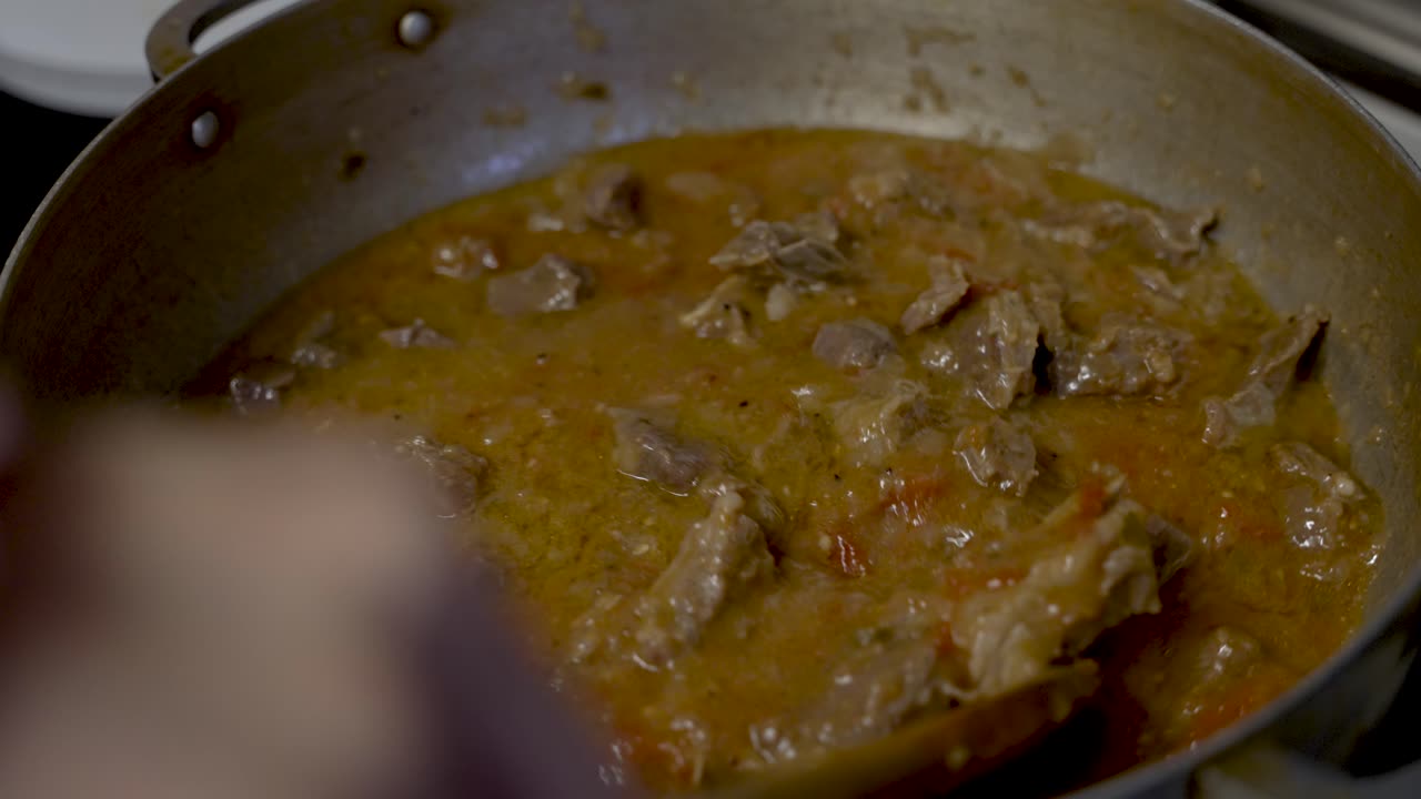 el curry de carne de res se agita con un cucharón de madera dentro de la sartén