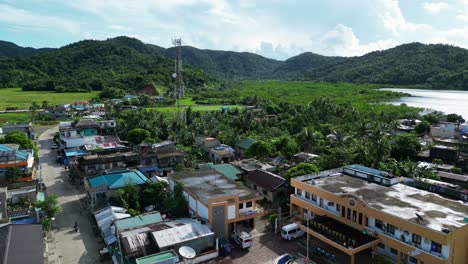 aerial dolly of picturesque filipino town center settlement with small buildings and satellite tower with lush mountains in background