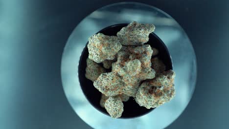 una macro cinematográfica de arriba hacia abajo movimiento suave de grúa toma de una planta de cannabis, cepas híbridas de naranja, tipo indica, flor de marihuana verde, cámara lenta 120 fps, luces de estudio, soporte giratorio brillante