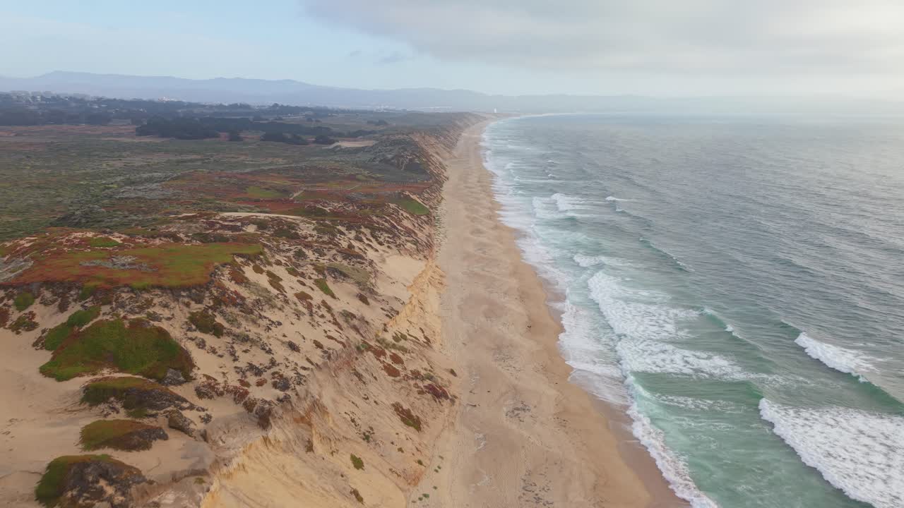 Drone tracking shot following Fort Ord Dunes with sand, vegetation and ocean waves on either side, Marina, California