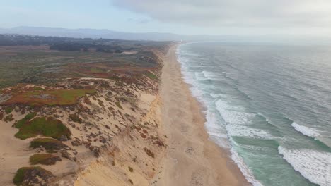 drone tracking shot following fort ord dunes with sand, vegetation and ocean waves on either side, marina, california