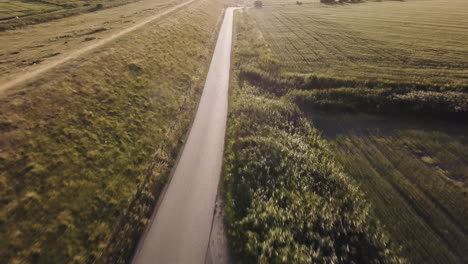 fast-drone-flight-backwards-above-an-empty-dyke-road,-back-light,-scenic-landscape,-sunset