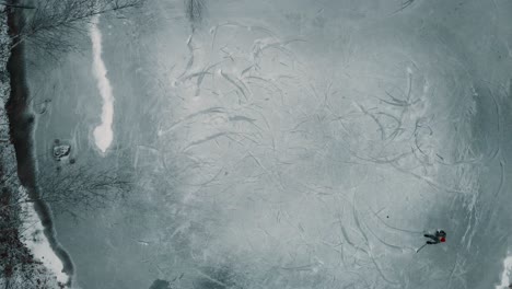 Drone-shot-flying-down-towards-a-single-player-playing-ice-hockey-on-a-frozen-pond-or-lake-in-Canada