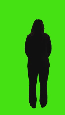 vertical video full length rear view silhouette shot of businesswoman wearing suit standing against green screen